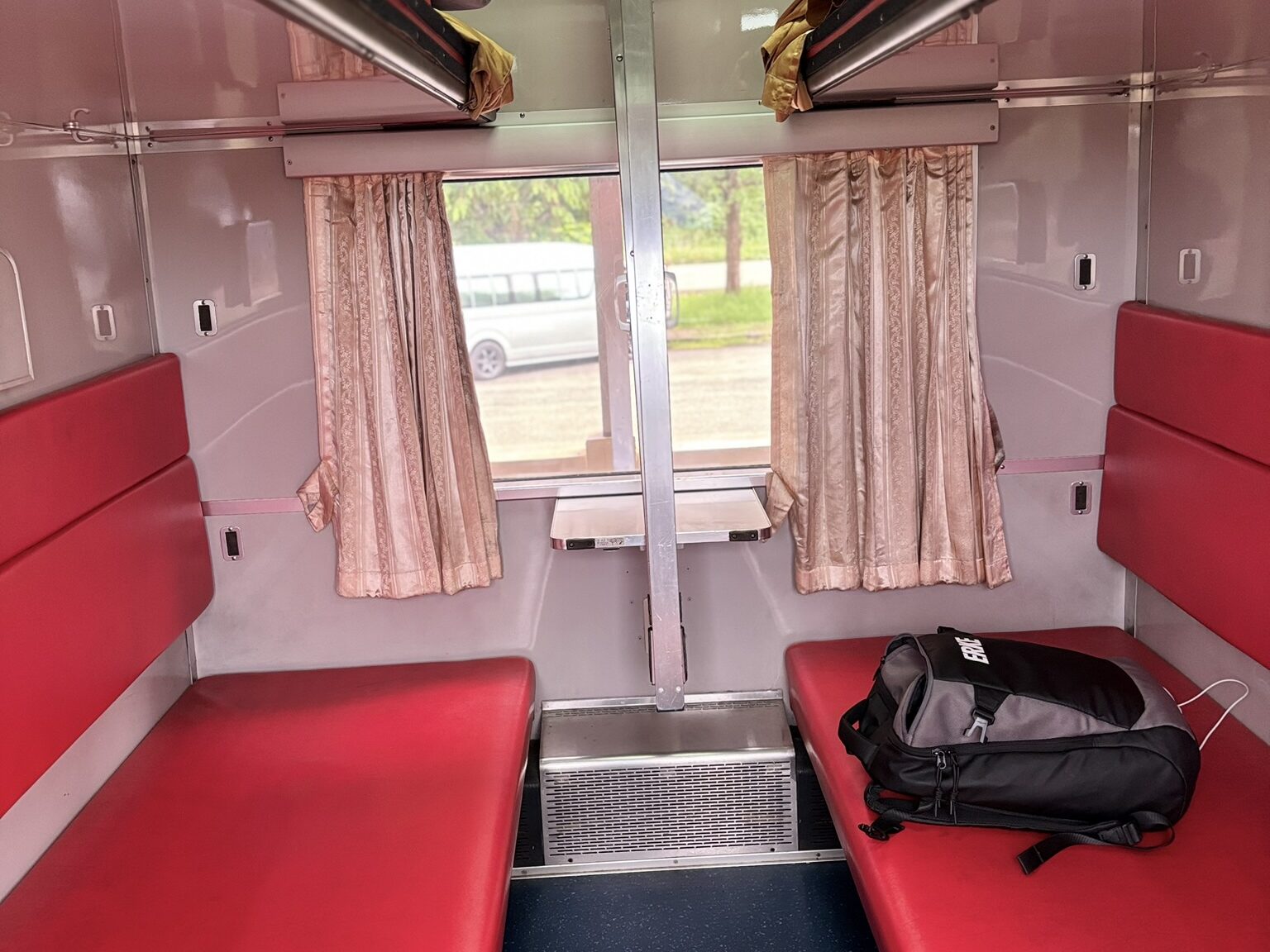 Second class AC sleeper berth interior on the Bangkok to Vientiane train showing red seats, upper and lower berths, curtains and window